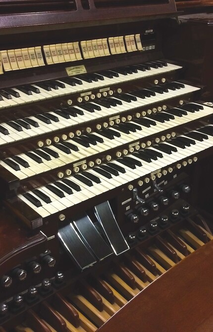 Close-up view of a dark wood organ, focusing on the keyboard, pedals, and knobs, showcasing its intricate design and craftsmanship.