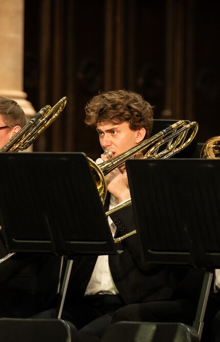Trombone section of an ensemble standing while performing, each musician focused and playing in unison, contributing to the overall sound of the group.