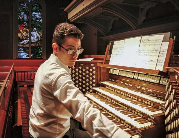 David Simon sits at an organ, with a stained glass window in the background.