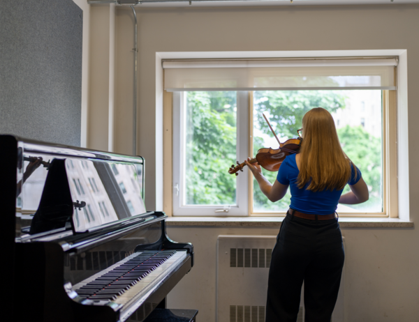 View of Elise from behind as she plays the violin while looking out the window.
