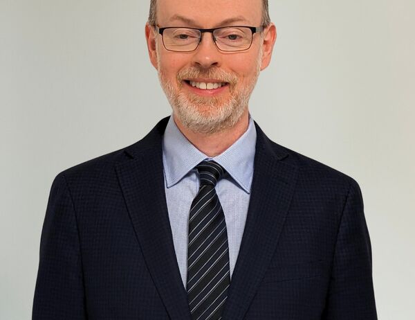 Man wearing a suit, smiling and standing in front of a white background.