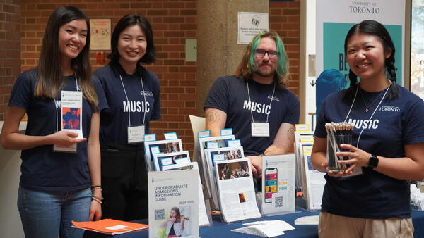 Thumbnail Image for 4 students standing behind an table filled with brochures.
