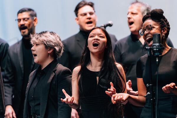 Thumbnail Image for Choir performing on stage in performance attire, emotionally singing into microphones, with expressions of passion and focus.