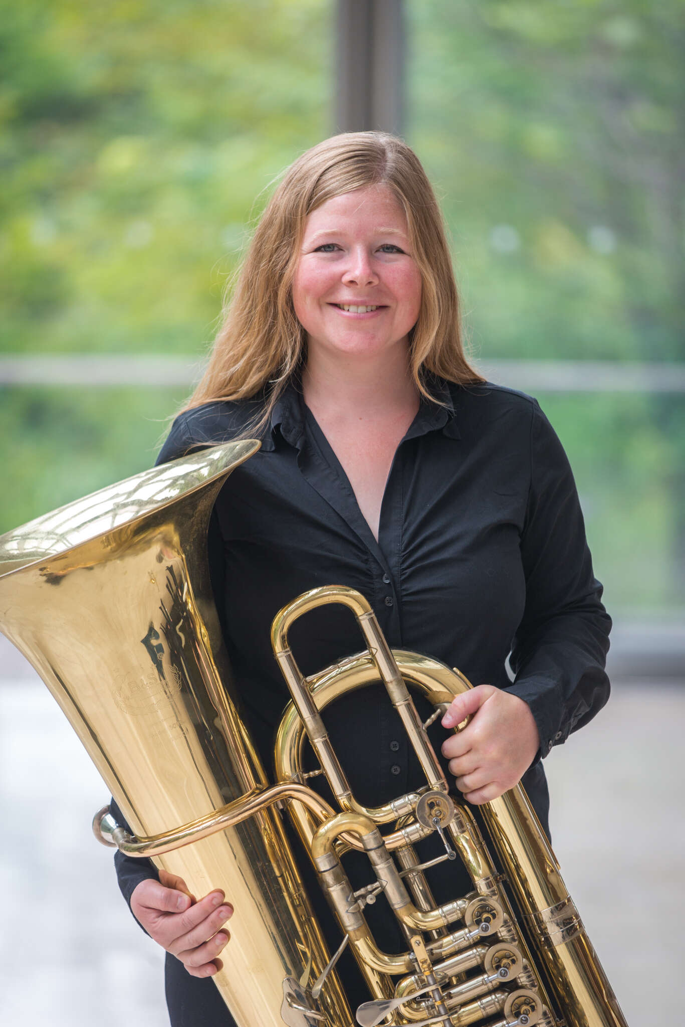 Professional portrait of Jennifer Stephen holding her tuba in front of a glass window.