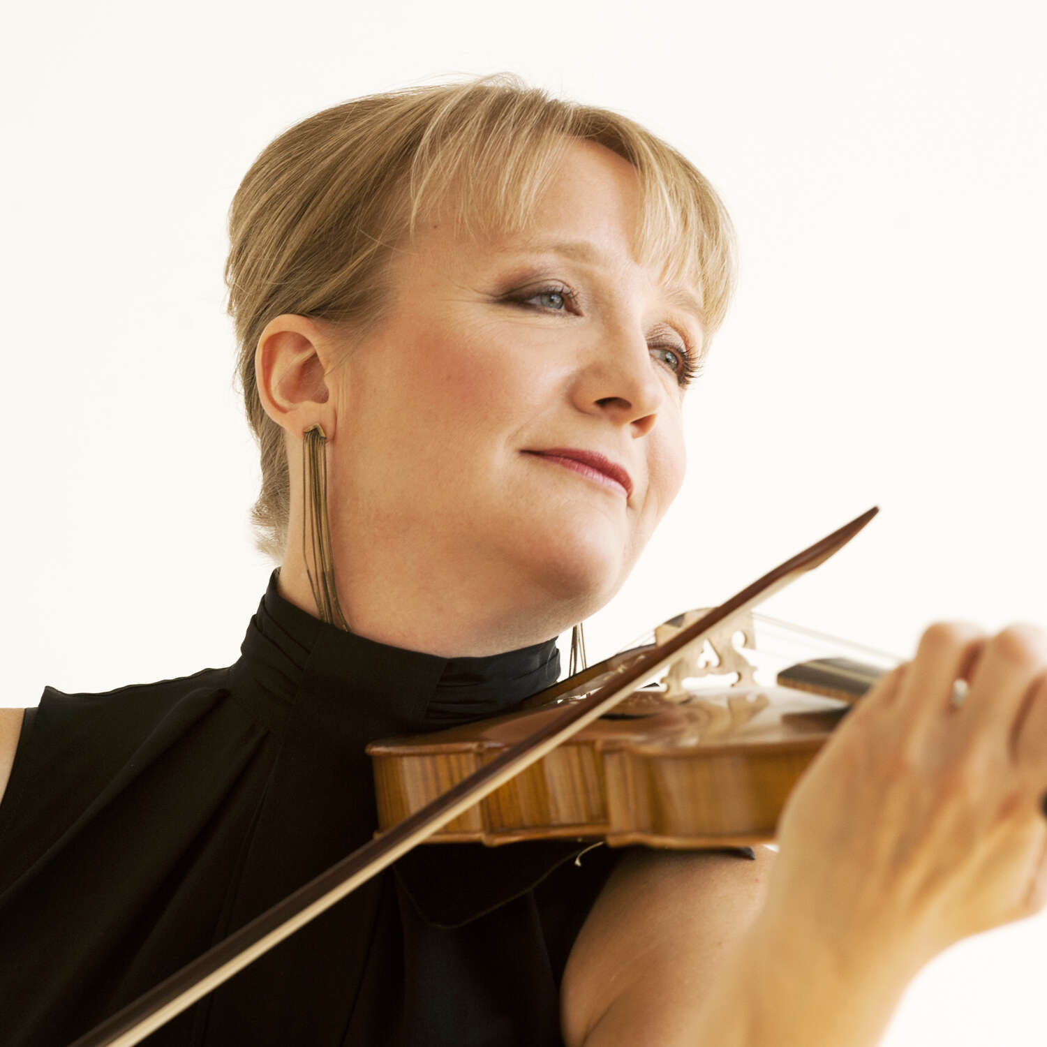 Professional portrait of Patricia Ahern looking to the side and playing her violin against a white backdrop.
