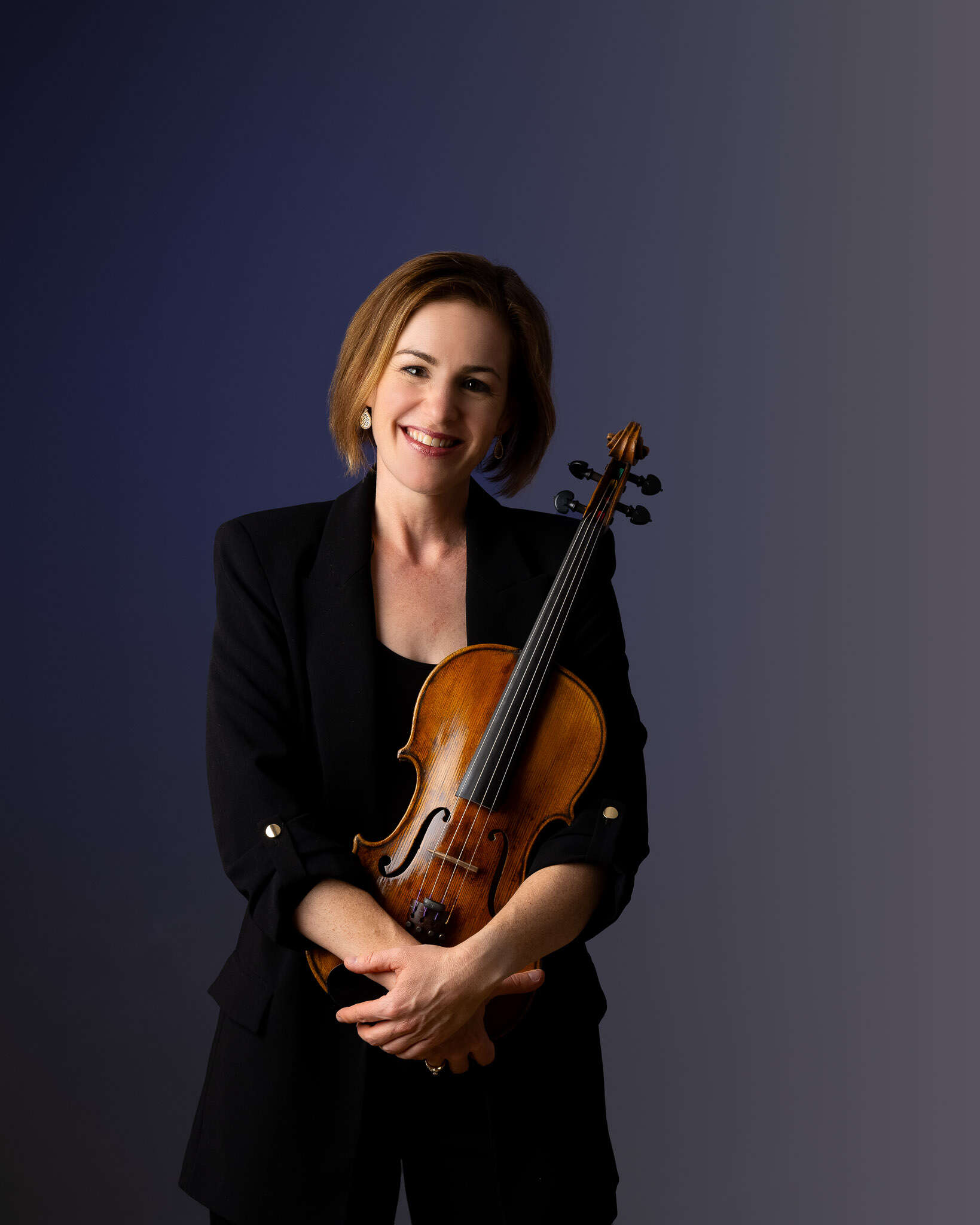 Professional portrait of Theresa Rudolph holding her viola against a dark blue backdrop.
