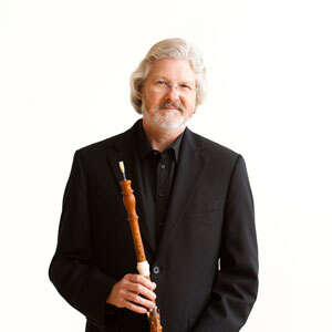 Professional headshot of John Abberger holding his oboe against a white backdrop.