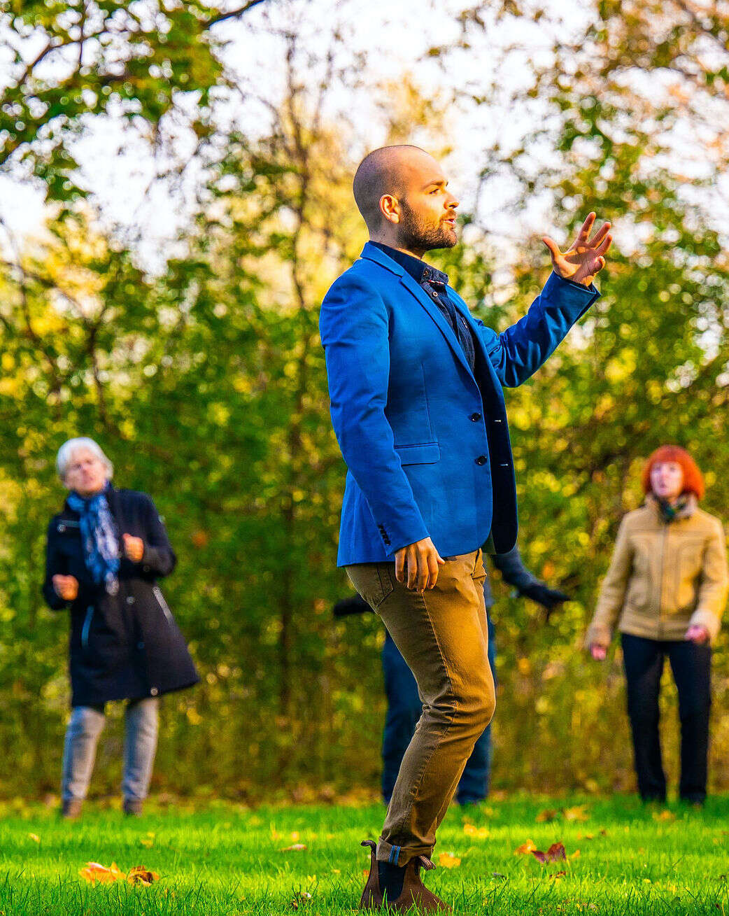 Photo of a person teaching a movement class outdoors, wearing a blue suit jacket.