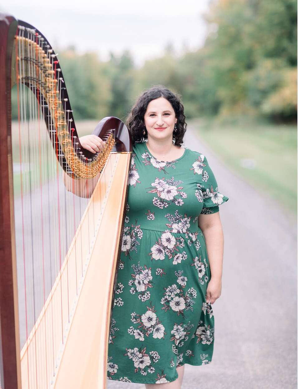 Person wearing a green dress standing with a harp on a scenic dirt road