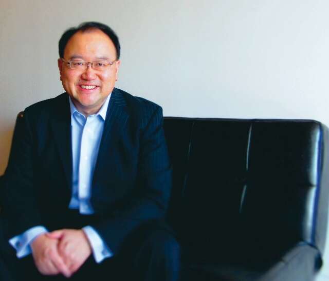 Andrew Kwan is sitting on a black chair, smiling. 