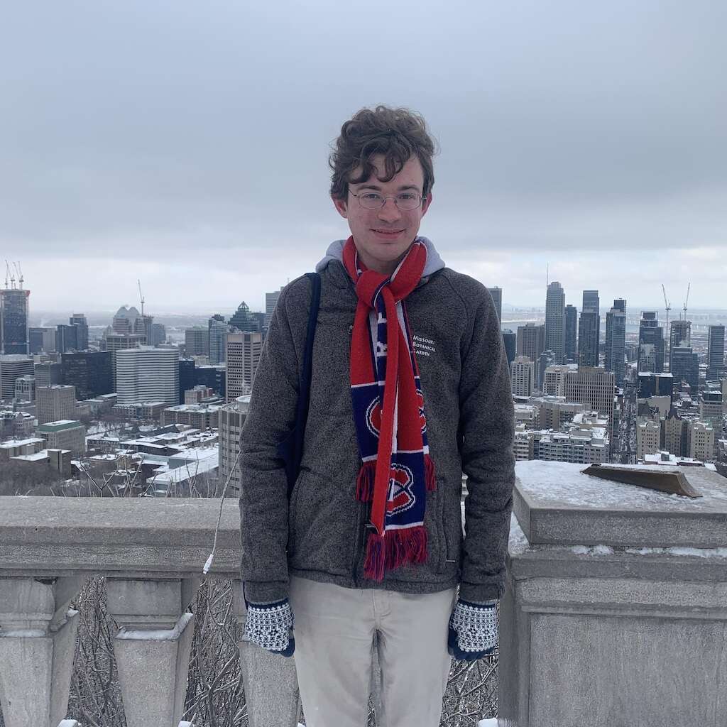 Person wearing winter gear smiling, standing in front of the Montreal skyline