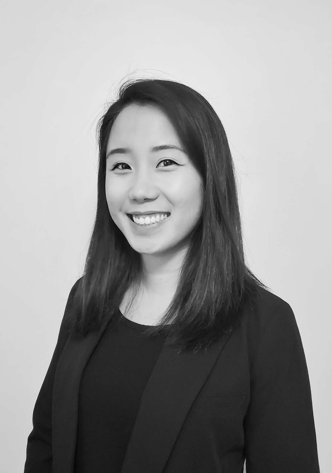 Black and white headshot of a person wearing all black, including a blazer, smiling confidently.