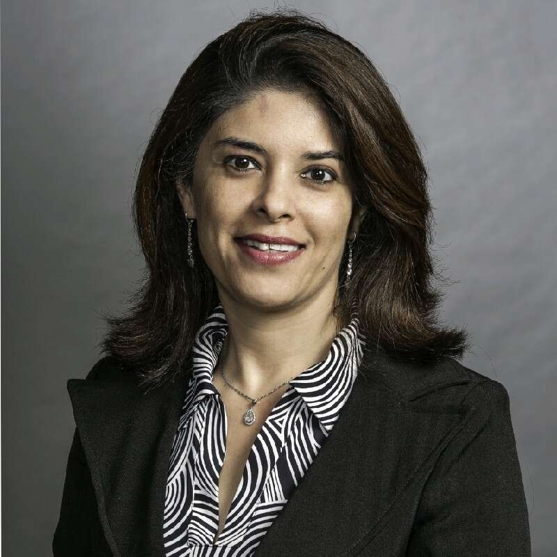 Headshot of a person wearing a striped shirt and blazer, smiling in front of a grey background.