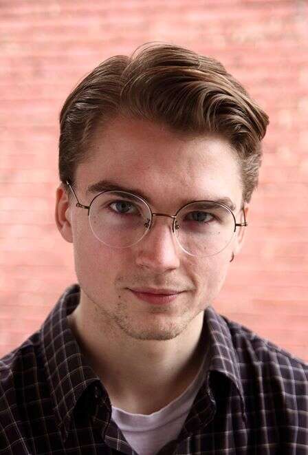 Headshot of person wearing glasses, blurred brick wall background