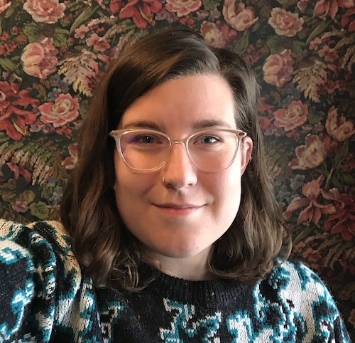 young person with glasses smiling, floral wallpaper in the background