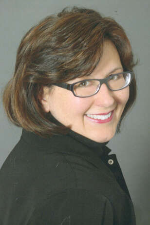 Person smiling warmly, looking over their shoulder while wearing a black shirt, with a grey background.