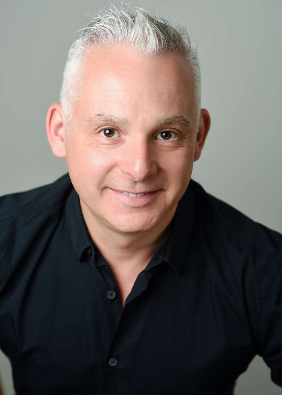 Headshot of a person wearing a black button-up shirt in front of a grey background, smiling.