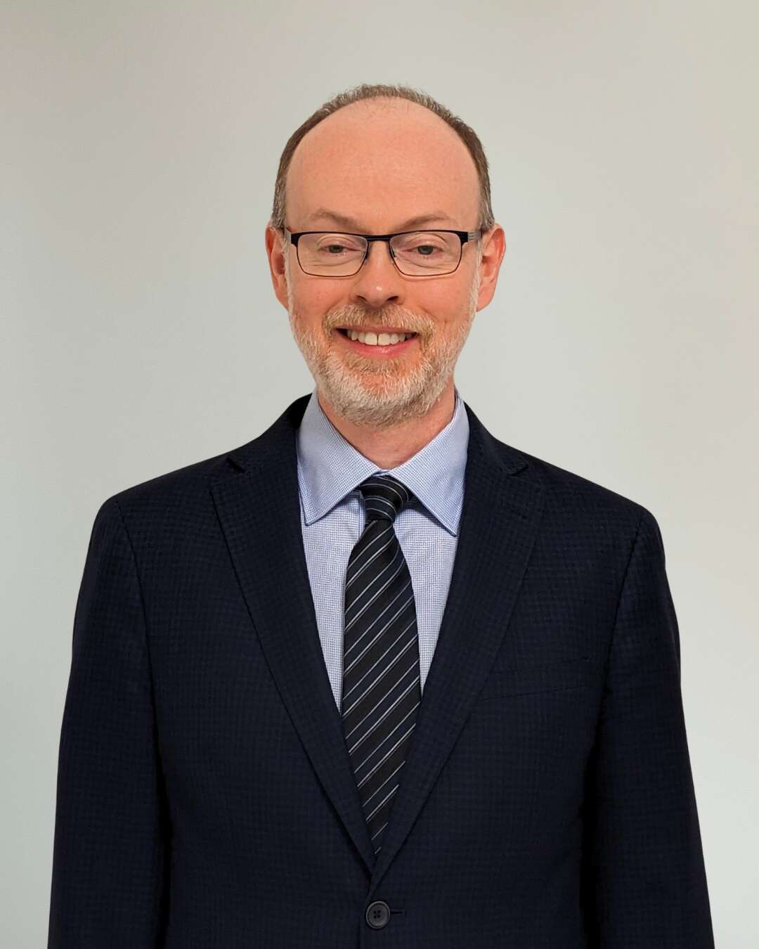 Man wearing a suit, smiling and standing in front of a white background.
