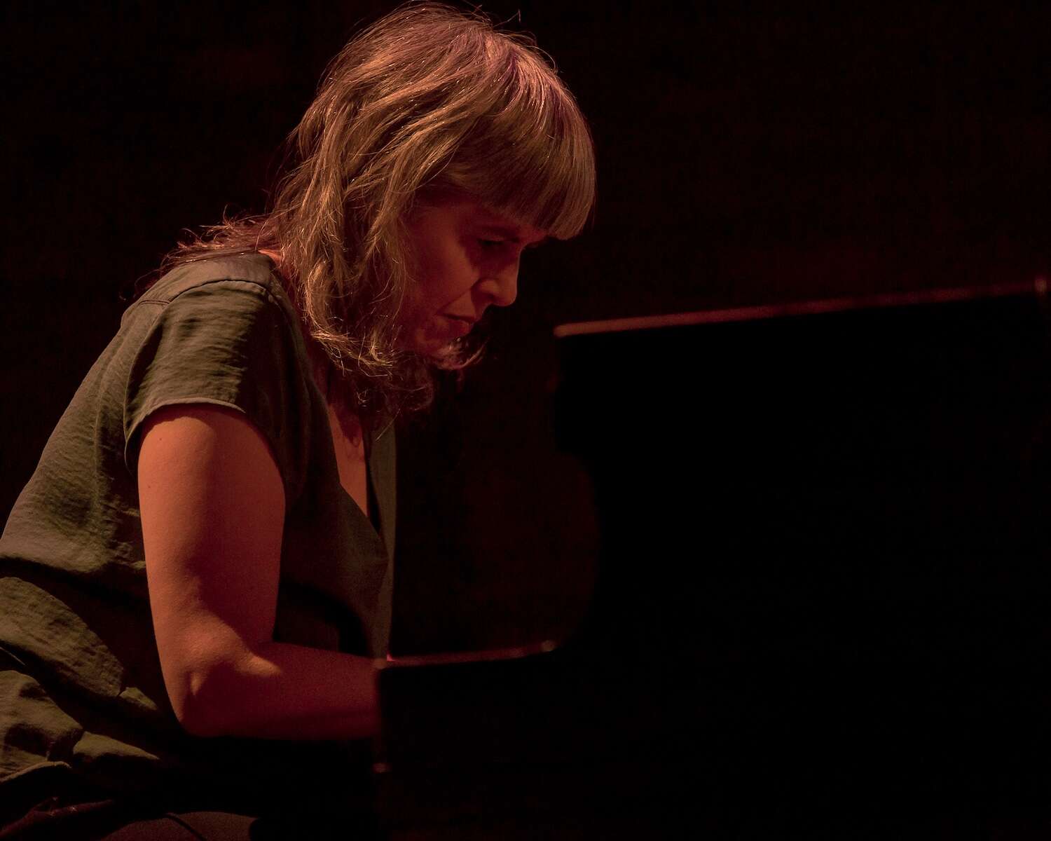 Person with bangs wearing a green shirt playing the piano, focused and concentrated.