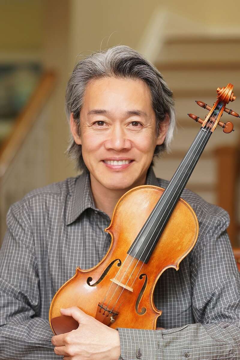 Person wearing a grey shirt, smiling while holding a violin.