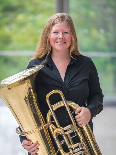 Professional portrait of Jennifer Stephen holding her tuba in front of a glass window.