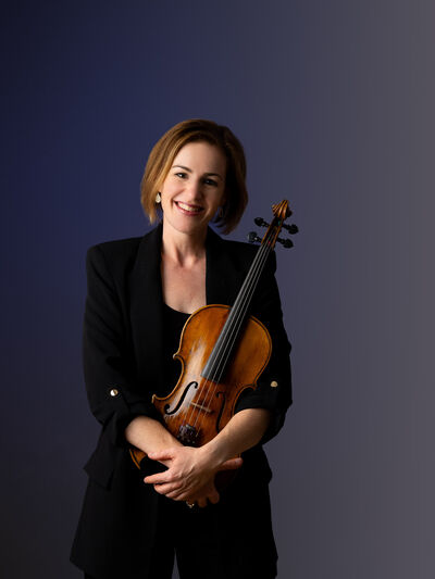 Professional portrait of Theresa Rudolph holding her viola against a dark blue backdrop.