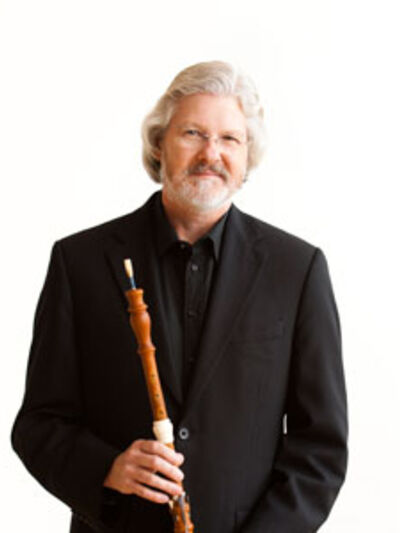 Professional headshot of John Abberger holding his oboe against a white backdrop.