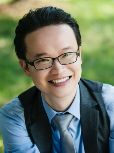 Professional headshot of Charles Lin, smiling and sitting on a bench with greenery behind him.