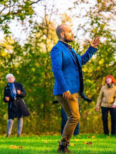 Photo of a person teaching a movement class outdoors, wearing a blue suit jacket.