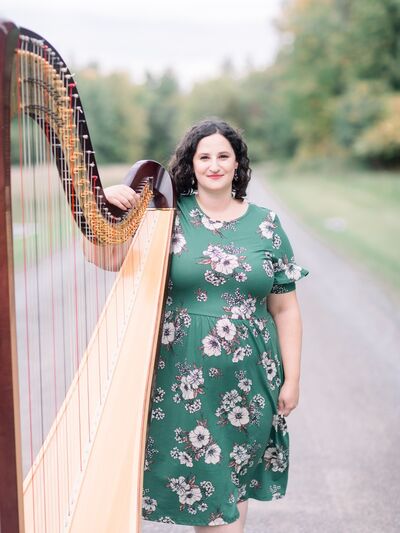 Person wearing a green dress standing with a harp on a scenic dirt road