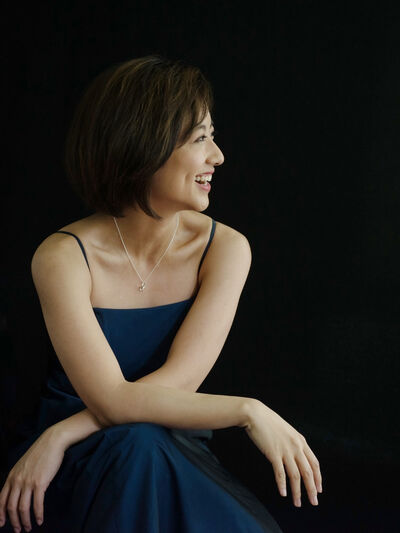 Person with short hair, wearing a blue dress, posed in front of a dark background.