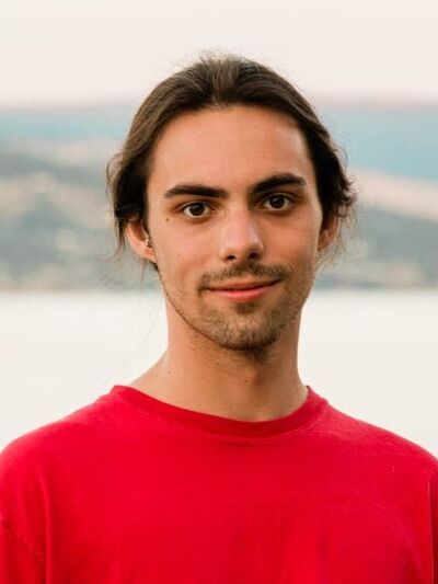 Young person wearing a red t-shirt standing in front of a lake 