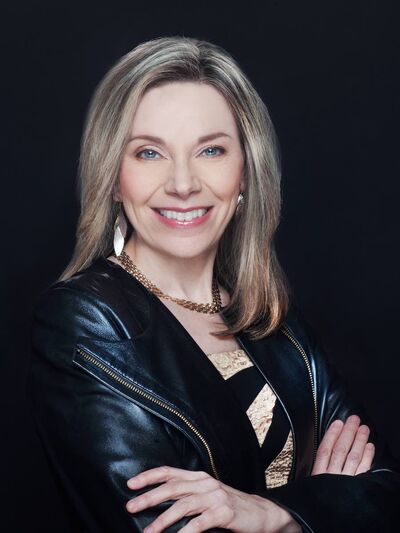 Professional headshot portrait of Rea Beaumont, who is smiling against a black backdrop