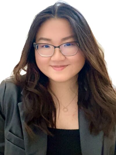 person with long hair wearing glasses and a blazer, smiling.