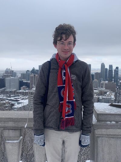 Person wearing winter gear smiling, standing in front of the Montreal skyline 