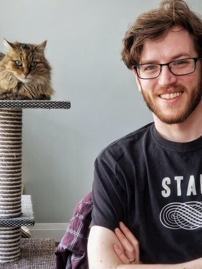 Picture of Colin Harris sitting down, arms crossed, smiling, with cat in the background.