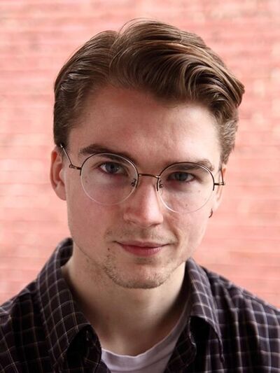 Headshot of person wearing glasses, blurred brick wall background