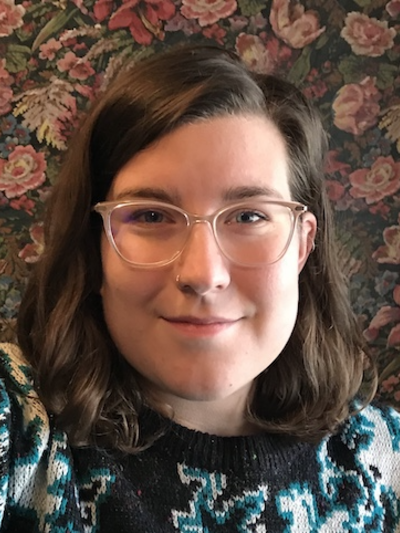 young person with glasses smiling, floral wallpaper in the background