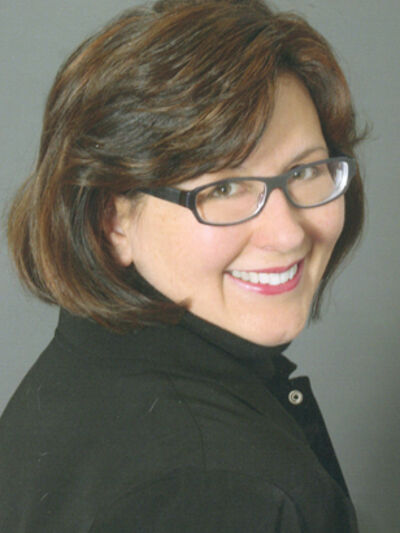Person smiling warmly, looking over their shoulder while wearing a black shirt, with a grey background.