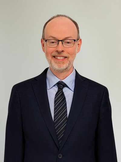 Man wearing a suit, smiling and standing in front of a white background.