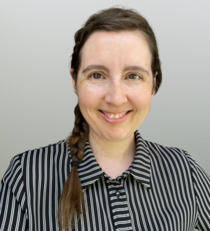Person with braided hair, wearing a striped shirt, smiling and looking directly at the camera