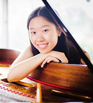 Person smiling posed with their head resting on their hands on a grand piano