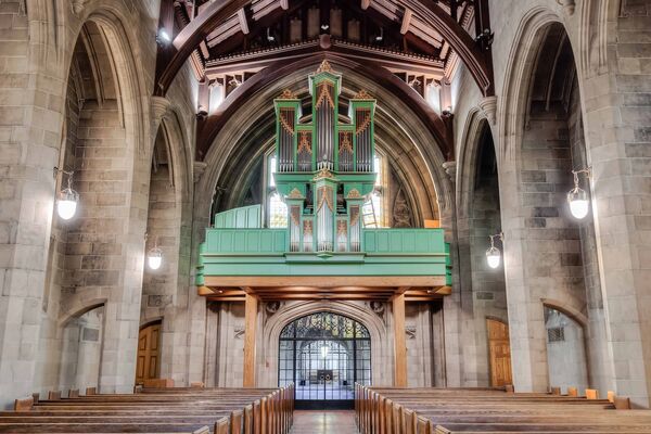 An organ in a church, showcasing its intricate pipes and green coloured wooden console, set against the backdrop of the church's interior with high ceilings.