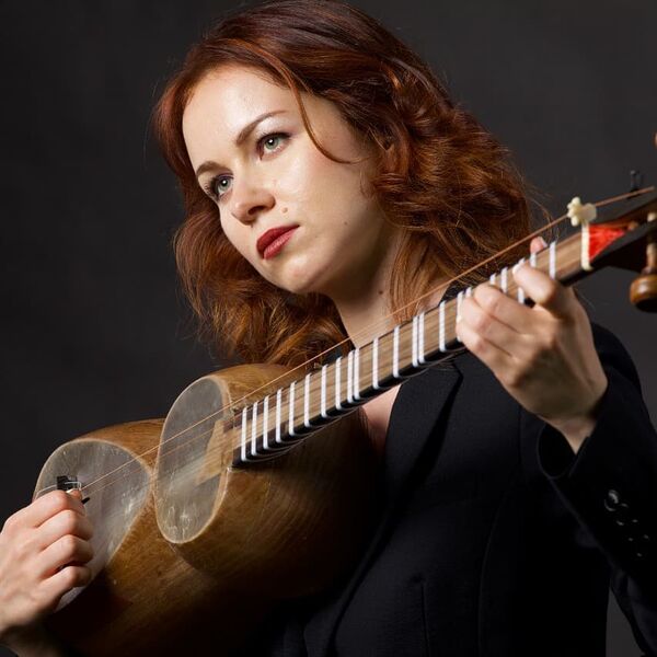 Person with red hair wearing black, holding a traditional Ukrainian instrument, set against a dark backdrop.