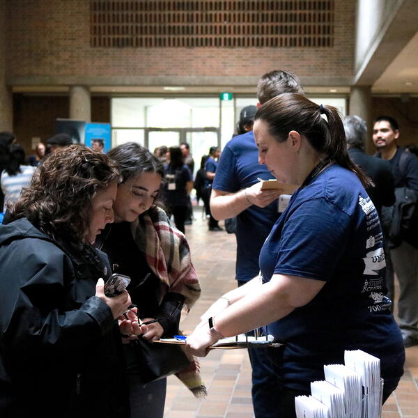 Female staff member talking to prospective student and mother reviewing information on a clipboard.