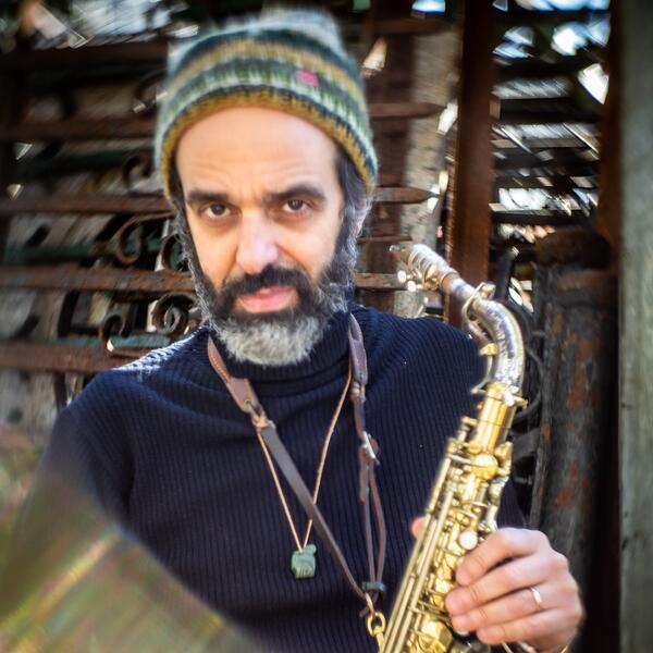 Michael Attias wearing a green and yellow hat while posing with a saxophone.