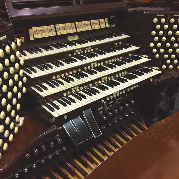 Close-up view of a dark wood organ, focusing on the keyboard, pedals, and knobs, showcasing its intricate design and craftsmanship.