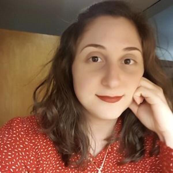 Headshot of a person wearing a red polka dot blouse, resting their hand gently on their face, with a warm and thoughtful expression.
