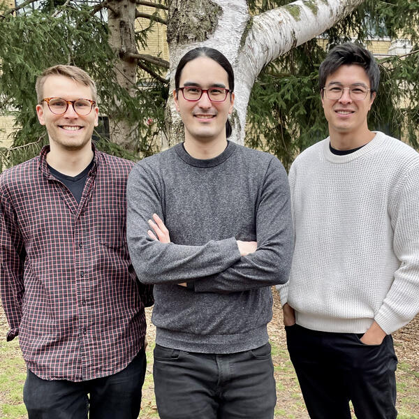 Three people with glasses smiling, standing outside in front of a tree