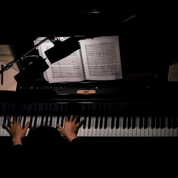 Overhead view of a person playing the piano in an orchestra pit, with their hands on the keys.
